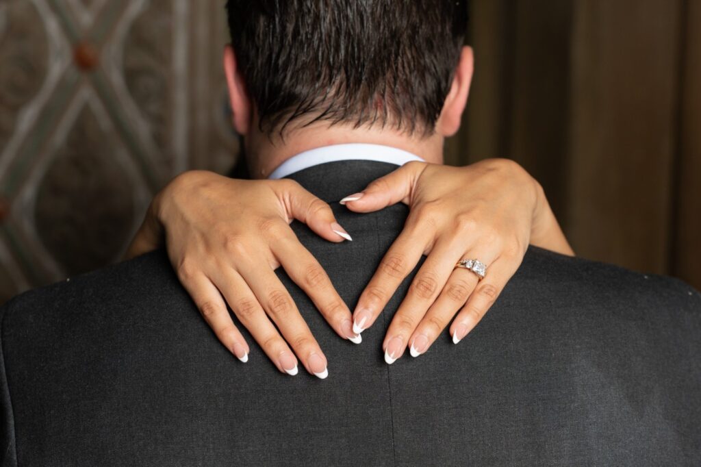 Close up of bride’s hands and engagement ring resting on groom’s shoulders during an intimate NYC elopement