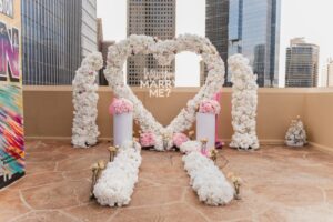 Houston rooftop proposal with luxury white floral heart arch, pink accents, and skyline views, perfect for romantic engagements
