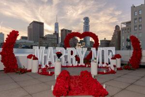 White "Marry Me" sign with "It Was Always You" light up sign with red roses, pathway candles, and the red roses are shaped in a heart