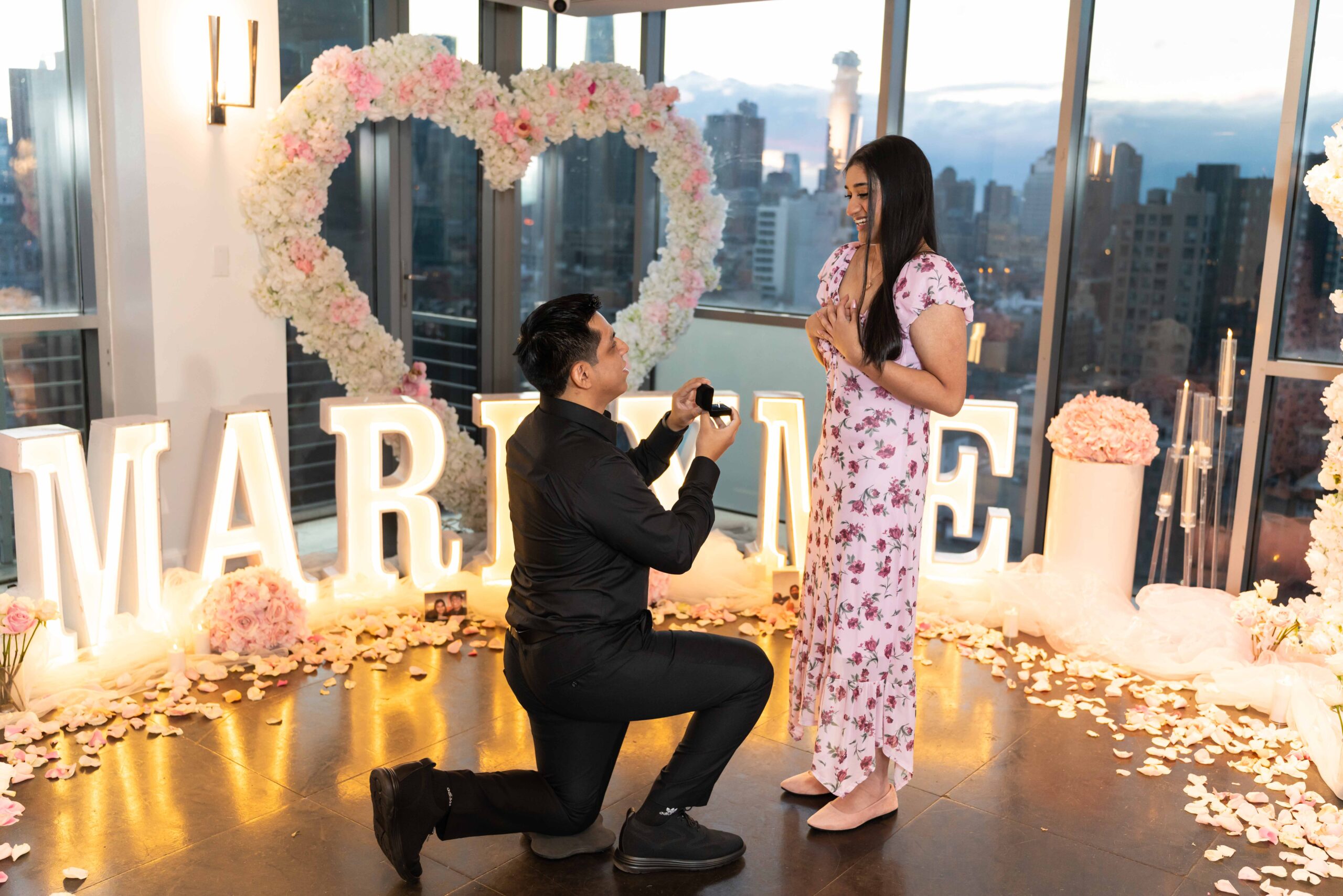 Indoor marriage proposal setup in NYC with Marry Me letters and a pink and white floral heart arch